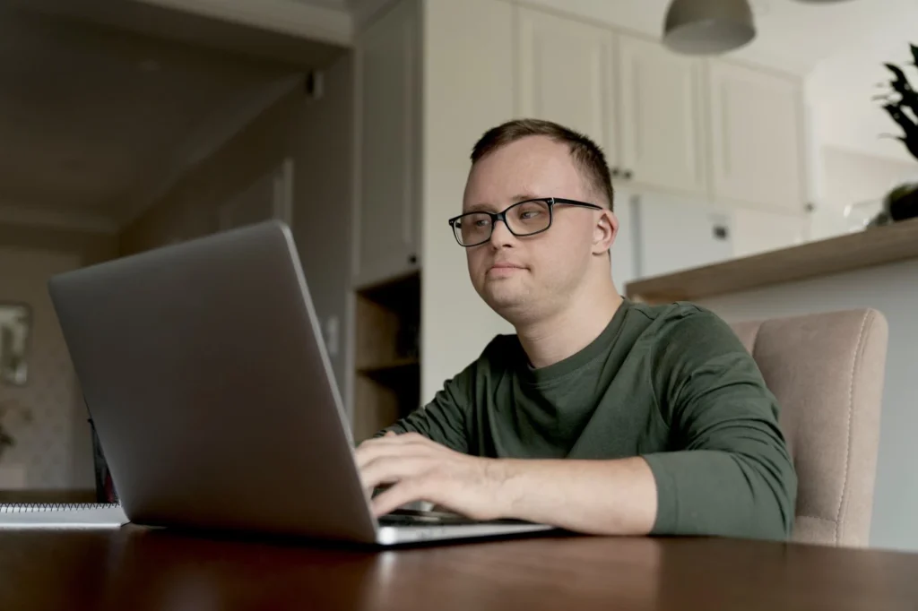 Disabled man with down syndrome using laptop at desk